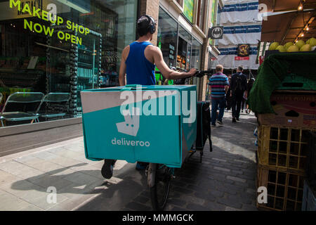 Un Deliveroo rider portant des écouteurs pousse son vélo dans un marché encombré Banque D'Images