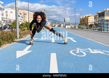 Jeune femme noire monter à cheval sur patins à l'extérieur, sur la ligne de vélo. Smiling girl avec coiffure afro à roues alignées sur un jour ensoleillé Banque D'Images