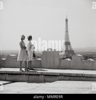 Années 1950, tableau historique par J Allan Paiement montrant deux élégantes dames françaises bien habillé debout sur un grand bâtiment, à la recherche sur les toits de la ville de Paris et la Tour Eiffel au loin. Banque D'Images