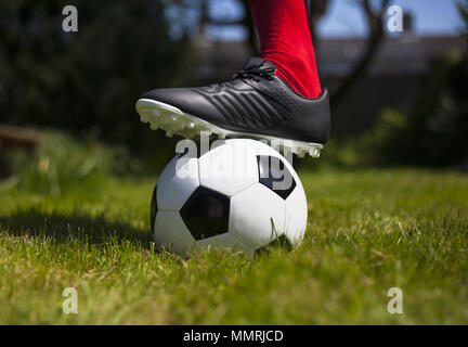 La jambe d'un joueur de football avec chaussette et démarrer sur un football en cuir noir et blanc Banque D'Images