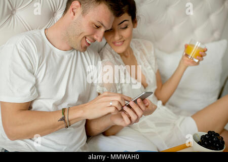 Couple aimant avoir un petit-déjeuner dans le lit et looking at mobile phone Banque D'Images