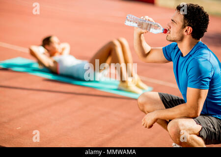 Jeune homme sportif de l'eau potable et de jeune femme faisant de l'exercice dans l'arrière-plan Banque D'Images