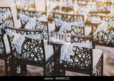 Un groupe de chaises en bois noir décoré avec de l'organza blanc ceinture fléchée pour Beach salle de mariage avant de commencer la cérémonie de mariage, thème de couleurs rétro Banque D'Images