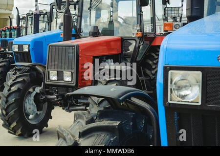 Machines agricoles, tracteurs se tenir dans une rangée de bleu et rouge. Nouveau groupe de machines avec les phares carrés Banque D'Images