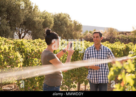 Brunette prend photo d'un homme en chemise à carreaux sur une belle journée dans le vignoble Banque D'Images