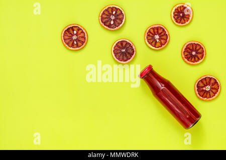 Beaux art fond alimentaire. En bouteilles en verre de jus rouge sang en tranches de fruits orange sur la surface d'un vert vif. Banque D'Images