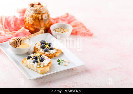 Crostini de pain grillé avec les baies fraîches blueberry et le miel, la ricotta, le thym et les noisettes, plus texturé en bois blanc. Vue de dessus, copiez l'espace. Banque D'Images