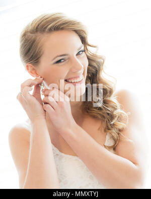 Une jeune mariée en blanc mise sur earring Banque D'Images