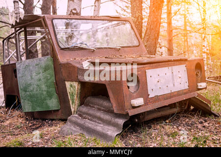 Close-up d'une vieille voiture jeep rouillée avec une porte cassée et pas de roues sur l'arrière-plan d'une forêt de conifères vert Banque D'Images