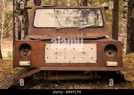 Close-up d'une vieille voiture jeep rouillée avec une porte cassée et pas de roues sur l'arrière-plan d'une forêt de conifères vert Banque D'Images