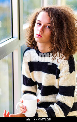 Cheveux bouclés avec mug teen girl sitting by window Banque D'Images