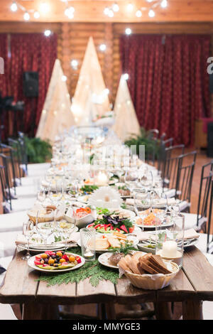 Mariage, salle à manger, de l'alimentation concept. sur la longue table en bois préparé pour les invités de la mariée et du fiancé il y a beaucoup de plats avec des friandises et de trans Banque D'Images