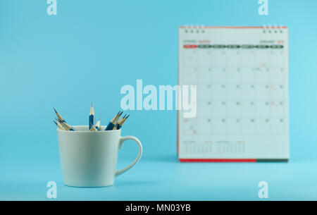 Crayons en blanc tasse avec calendrier sur fond bleu Banque D'Images