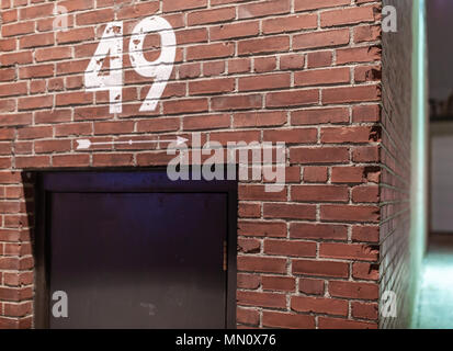 Numéro 49 peint sur un mur de briques avec une flèche blanche peinte sur le côté point du bâtiment industriel au-dessus d'une porte noire Banque D'Images