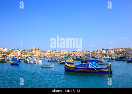 Malte, Marsaxlokk port historique plein de bateaux. Destination pour les vacances, la détente et la pêche. Le ciel bleu et le village historique. Banque D'Images