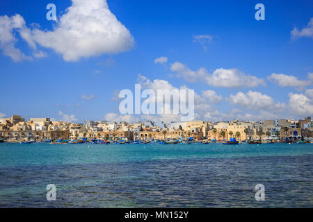 Marsaxlokk port historique plein de bateaux dans Malte. Ciel bleu avec quelques nuages blancs et le village historique. Destination pour les vacances, se détendre et de la pêche Banque D'Images