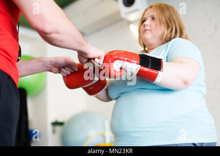 Low angle portrait de jeune femme obèse fist bumping avec entraîneur personnel de conditionnement physique au cours de la formation en salle de sport, copy space Banque D'Images