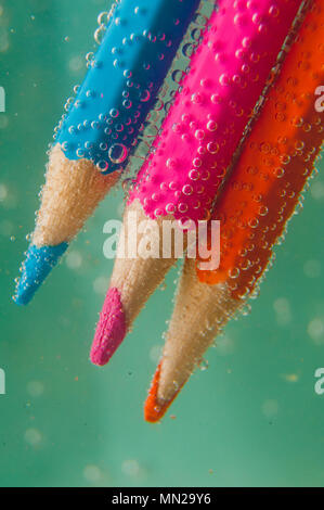 Crayons de couleur dans l'eau avec des bulles sur un fond bleu Banque D'Images