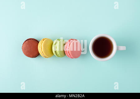 Une tasse de café avec quatre macarons colorés sur fond bleu turquoise. Style minimal de mise à plat avec place pour texte, vue d'en haut. Banque D'Images