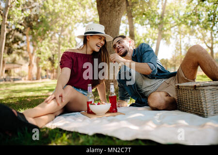 Smiling young man and woman sitting on picnic blanket et avoir du plaisir. Cheerful young couple at picnic. Banque D'Images