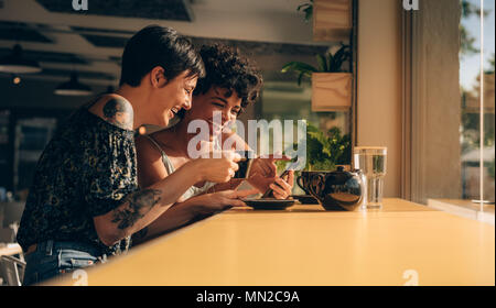 Deux femmes à l'aide de téléphone mobile et de boire du café au café les femmes passent leur temps libre au café. Banque D'Images