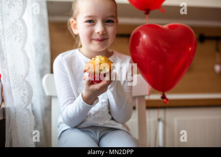 Cute girl bambin célébrer 6e anniversaire. Girl eating her birthday cupcake dans la cuisine, entouré par des ballons. Banque D'Images