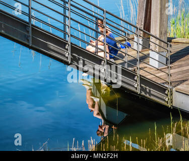 Britzer Garten, Neukölln, Berlin, Allemagne. 2018.jeune couple s'asseoir à côté de soleil rhizomatiques pont sur traquil lake Banque D'Images