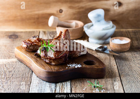 Côtelettes de veau grillées aux herbes sur la planche à découper en bois rustique, pan steak poêlé Banque D'Images