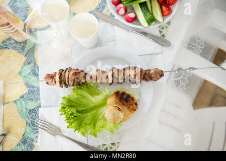 De la viande barbecue pique-nique sur brochette, lunettes, et les verts. Grillades de viande et l'oignon sur la table avec des légumes. Banque D'Images