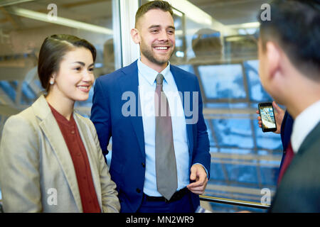 Waist up portrait of smiling couple in businesswear parlant à ami holding smartphone et la prise de photo Banque D'Images
