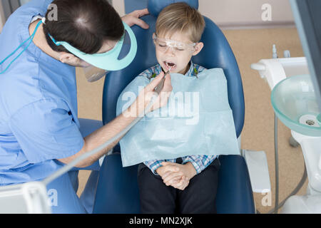 Portrait de petit garçon assis dans un fauteuil dentaire dentiste dents alors que son traitement et le remplissage de cavité clinique moderne Banque D'Images