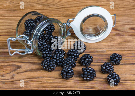 Les mûres renversé sur un fond de bois. Belle close-up de délicieux rafraîchissements juteuse de fruits fruité noir dans un bocal en verre sur la table de jardin. Banque D'Images