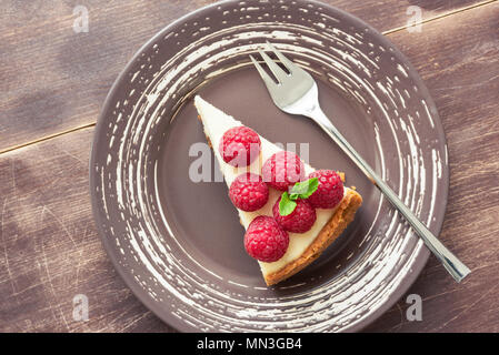 Tranche de gâteau au fromage garni de framboises fraîches et de feuille de menthe sur fond de bois. Vue d'en haut. New York Cheesecake aux fruits rouges Banque D'Images