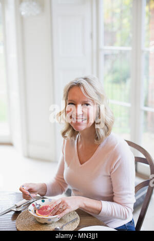 Portrait of smiling mature woman eating grapefruit Banque D'Images