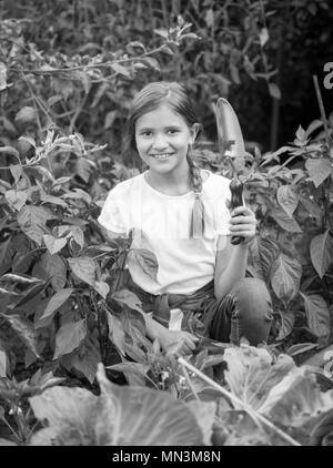 Le noir et blanc portrait of smiling teenage girl sitting in garden et truelle holding Banque D'Images