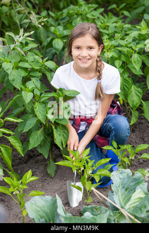 Portrait of beautiful smiling girl du forage jardin lit avec la culture de légumes avec une truelle à encoches Banque D'Images