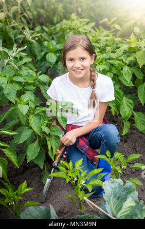 Portrait de belle jeune fille assise dans le jardin et du forage du sol, avec la culture de légumes Banque D'Images