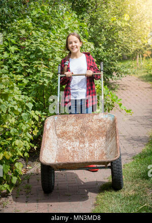 Smiling teenage Girl in red rubber boots tirant whellbarrow jardin Banque D'Images