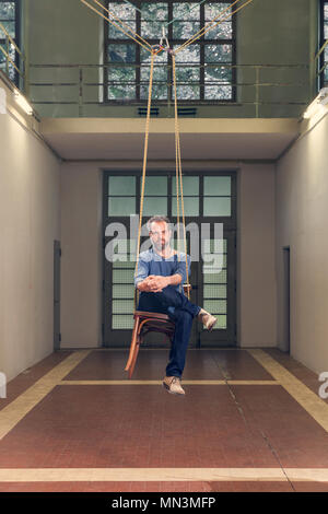 Homme assis sur un fauteuil suspendu, de l'intérieur Banque D'Images