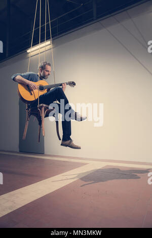 Homme assis sur un fauteuil suspendu joue de la guitare, de l'intérieur Banque D'Images