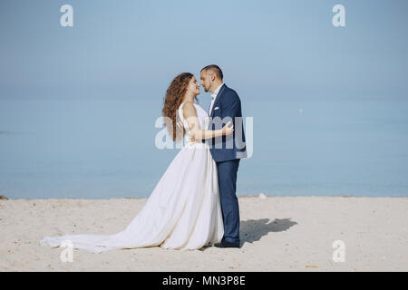 Belle jeune femme aux cheveux longs en robe blanche avec son jeune mari sur la plage Banque D'Images