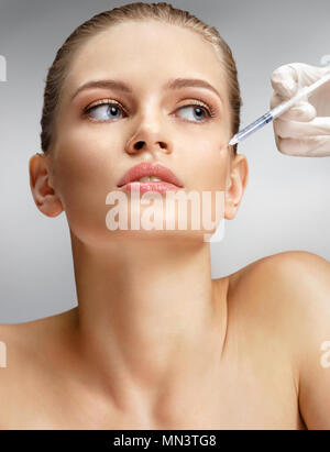 Belle femme recevant botox injection dans la joue de l'esthéticienne. Portrait of young woman getting beauté injections faciales sur fond gris. Nettoyer Banque D'Images