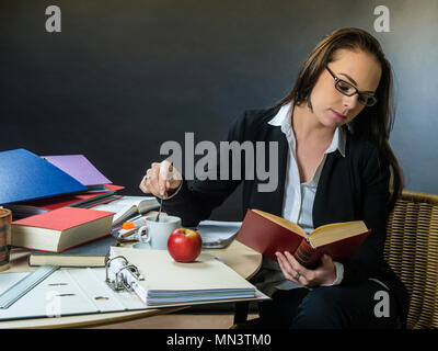 Photo d'un enseignant ou d'affaires femme d'une 30 ans assis à un bureau devant un grand tableau noir lecture. Banque D'Images
