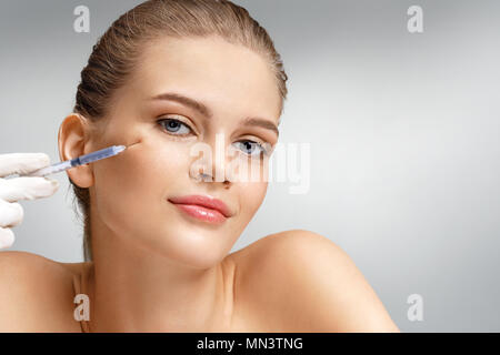 Belle femme recevant botox injection dans la joue de l'esthéticienne. Portrait of young woman getting beauté injections faciales sur fond gris. Nettoyer Banque D'Images