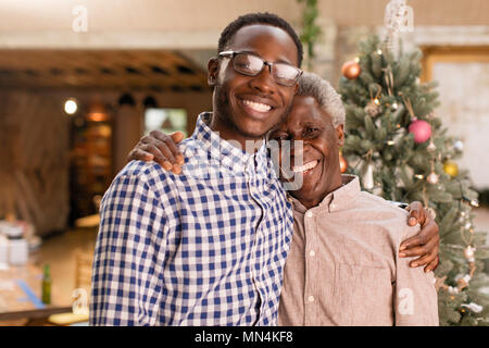 Portrait smiling grandfather and grandson hugging in front of Christmas Tree Banque D'Images