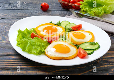 Œuf frit dans un cercle de poivrons doux sur une plaque blanche avec des légumes frais sur un fond de bois. Délicieux petit déjeuner sain. Une bonne nutrition. Banque D'Images