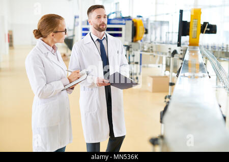 Deux inspecteurs des vêtements blancs manteaux holding notepad et presse-papiers en mains dans l'exercice de contrôle de la qualité au ministère de l'usine laitière de l'emballage Banque D'Images