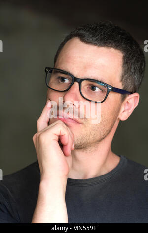 Portrait of young handsome stern black-haired man intellectuelle fructueuse non rasé confiant dans les verres avec des yeux noir brillant à pensivement je Banque D'Images