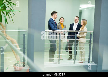 Portrait de quatre personnes debout dans le hall de l'immeuble de bureaux modernes à discuter joyeusement, copy space Banque D'Images