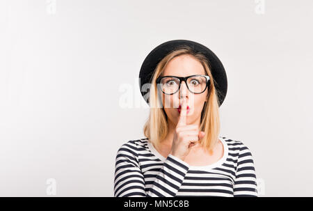 Portrait d'une belle jeune femme avec un chapeau noir en studio, mettant un doigt sur sa bouche. Copier l'espace. Banque D'Images